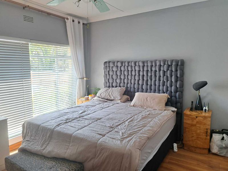 A well-lit bedroom featuring laminate flooring, a ceiling fan, and venetian blinds, providing a comfortable and functional living space.