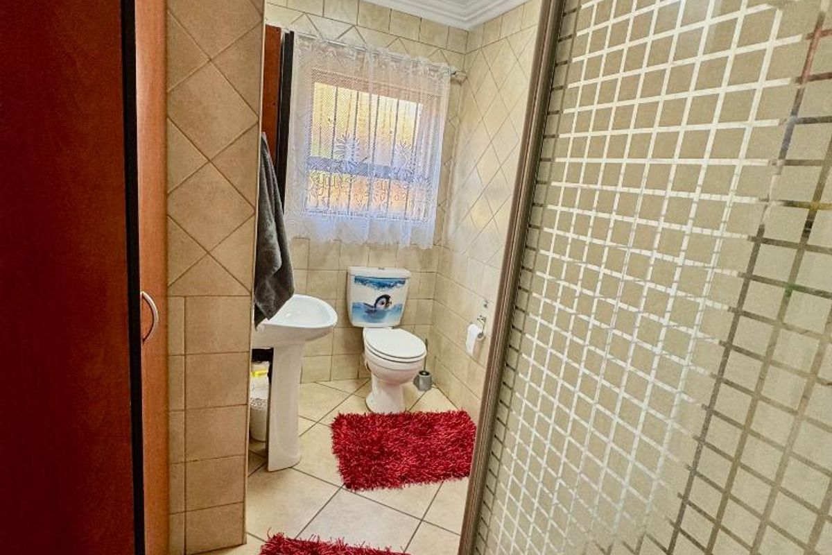 A functional bathroom featuring a pedestal basin, toilet, and a shower enclosure with a patterned glass door, finished with neutral wall and floor tiles.