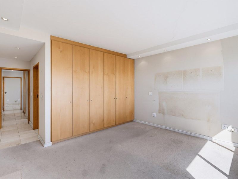 An empty bedroom featuring built-in wooden cupboards, recessed lighting, and carpeted flooring, requiring minor wall and ceiling repairs.