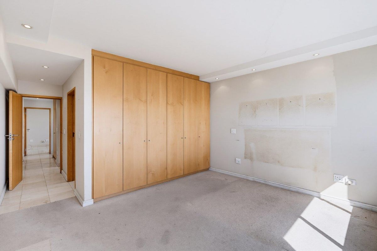 An empty bedroom featuring built-in wooden cupboards, recessed lighting, and carpeted flooring, requiring minor wall and ceiling repairs.