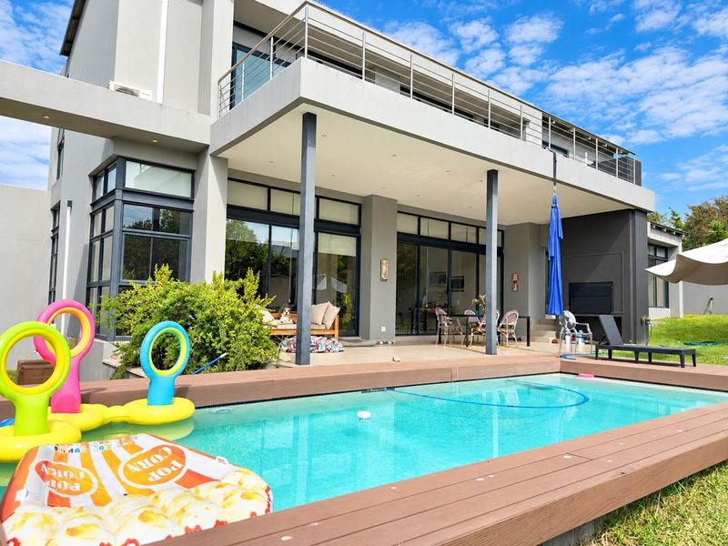 Modern double-story home featuring a swimming pool with composite decking, a spacious covered patio, and an upper-level balcony with stainless steel railings.