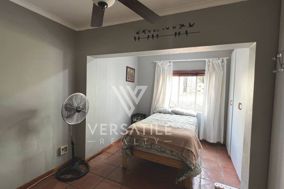A bedroom featuring tiled flooring, built-in cupboards, and a ceiling fan, offering a functional space with natural light.