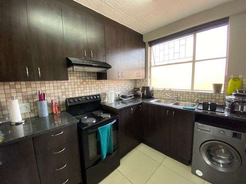A functional kitchen featuring dark wood cabinetry, granite countertops, a mosaic tile backsplash, and integrated space for a washing machine.