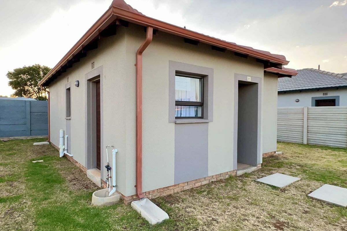 A view of the exterior rear of a compact residential unit featuring plastered walls, tiled roof, and external plumbing fixtures.