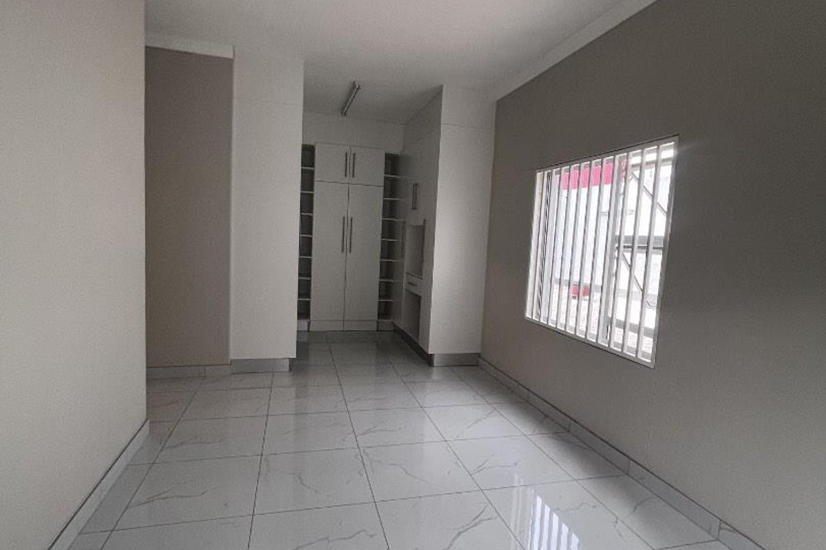 A bright, empty bedroom featuring modern white marble-look floor tiles, built-in storage cupboards, and security bars on the window.