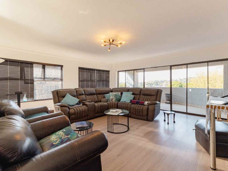Spacious living room featuring light-toned laminate flooring, modern ceiling lighting, and large sliding glass doors providing access to an outdoor balcony area.