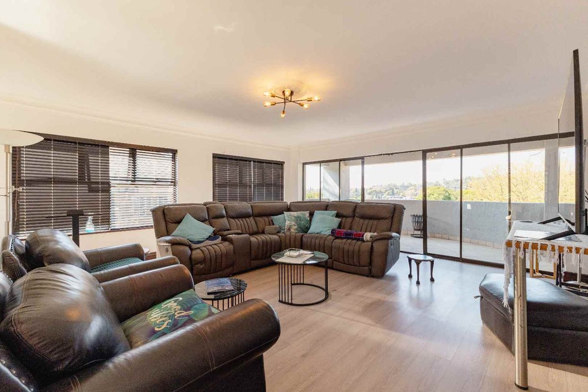 Spacious living room featuring light-toned laminate flooring, modern ceiling lighting, and large sliding glass doors providing access to an outdoor balcony area.