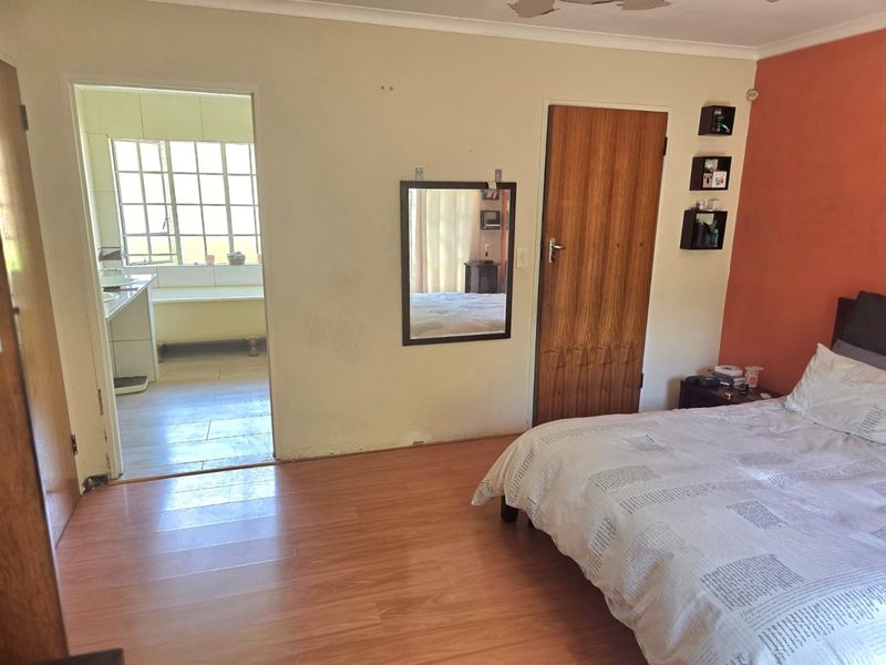 Bedroom featuring laminate flooring and an adjoining en-suite bathroom, showing signs of wear on the ceiling and walls.