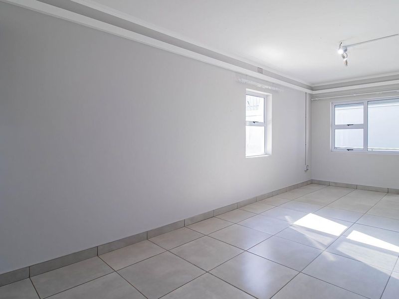 A bright, empty living area featuring neutral tiled flooring, coved ceiling cornices, and access to an outdoor space through a sliding glass door.
