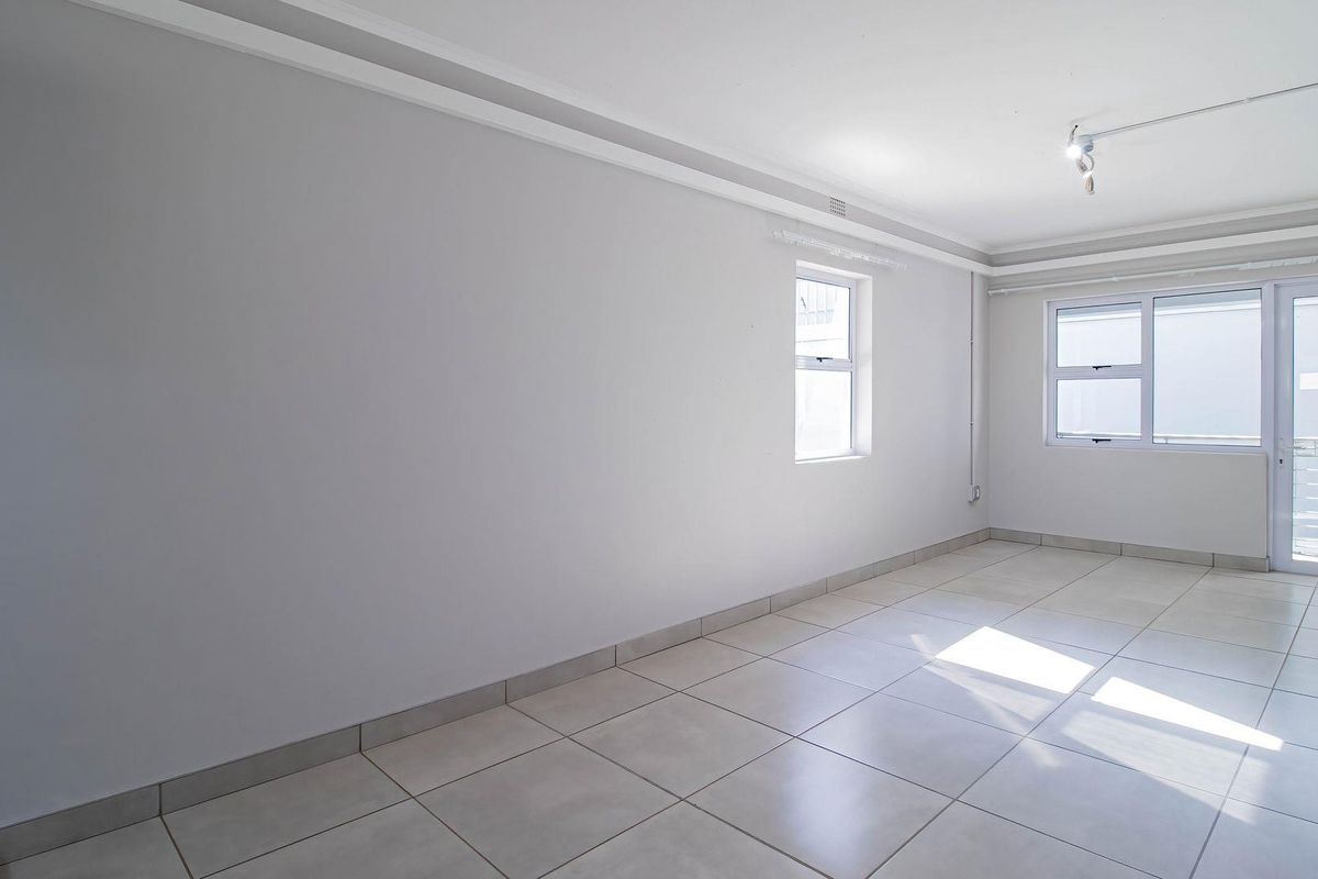 A bright, empty living area featuring neutral tiled flooring, coved ceiling cornices, and access to an outdoor space through a sliding glass door.