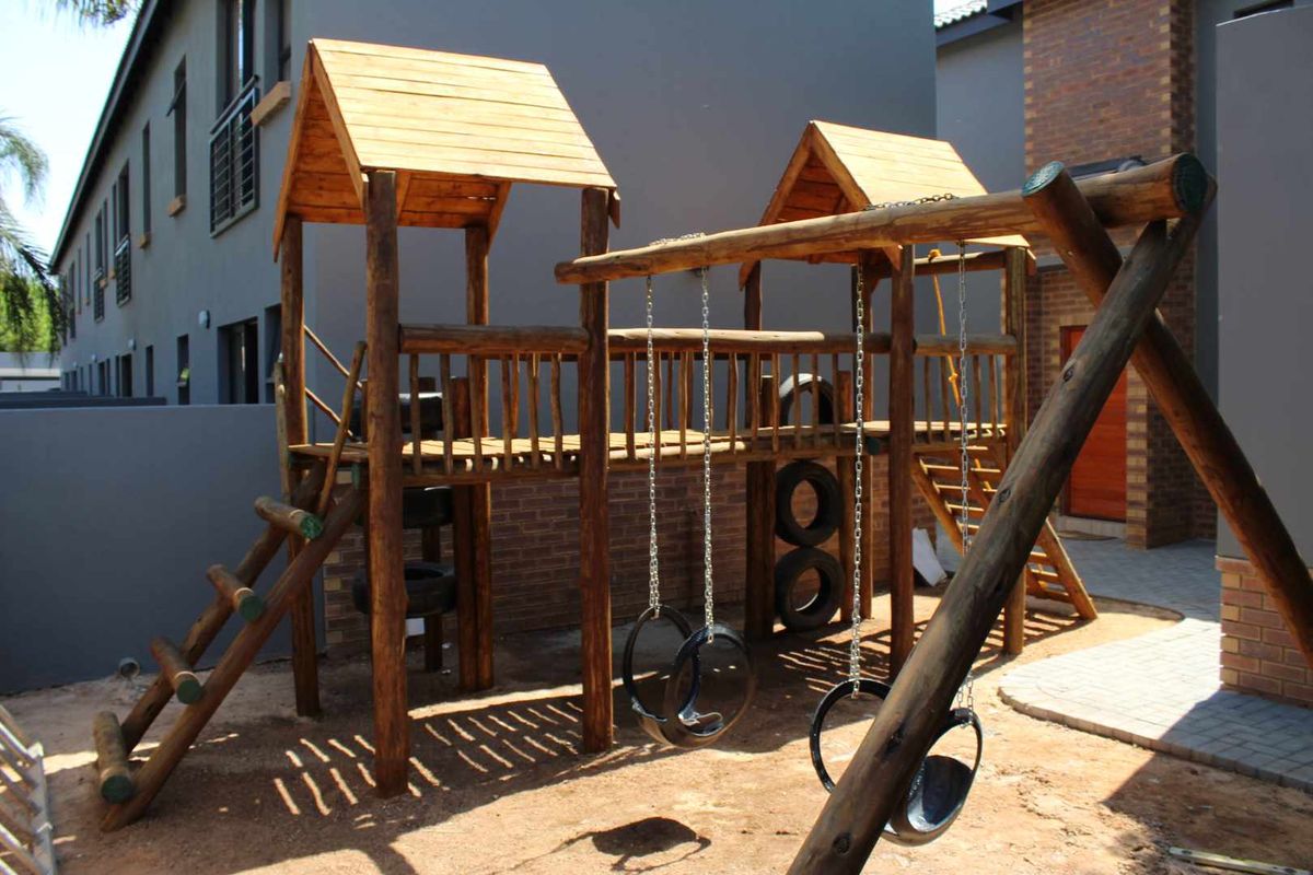 A communal outdoor area featuring a wooden playground structure with swings, set against the brick and rendered facade of an apartment complex.
