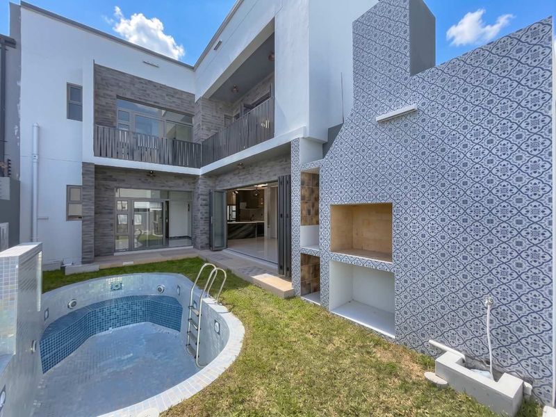 Modern rear exterior featuring a swimming pool, a decorative tiled built-in braai, and seamless indoor-outdoor flow through large stacking doors to the living area.