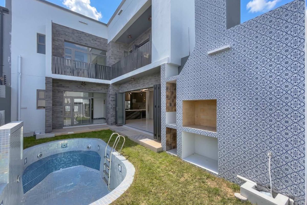 Modern rear exterior featuring a swimming pool, a decorative tiled built-in braai, and seamless indoor-outdoor flow through large stacking doors to the living area.
