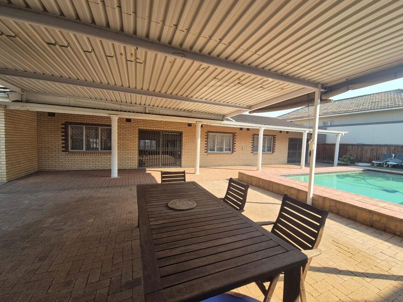 Spacious covered patio area featuring brick paving, a corrugated metal roof, and direct access to an adjacent swimming pool.