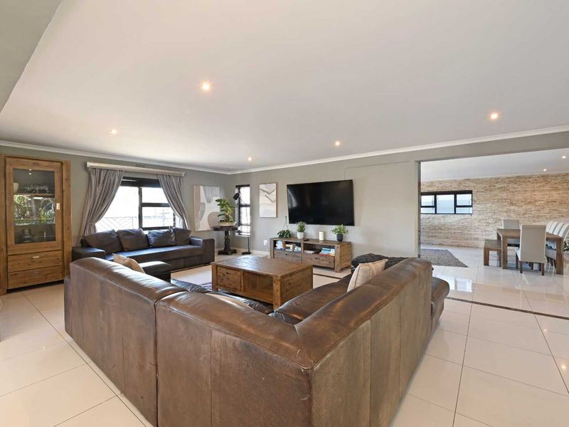 Spacious open-plan living and dining area featuring polished tiled flooring, recessed downlighting, and a decorative stone feature wall in the dining section.