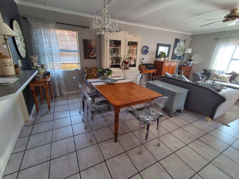 Open-plan living and dining area featuring tiled flooring, a ceiling fan, and a decorative chandelier, providing a versatile space for daily living.