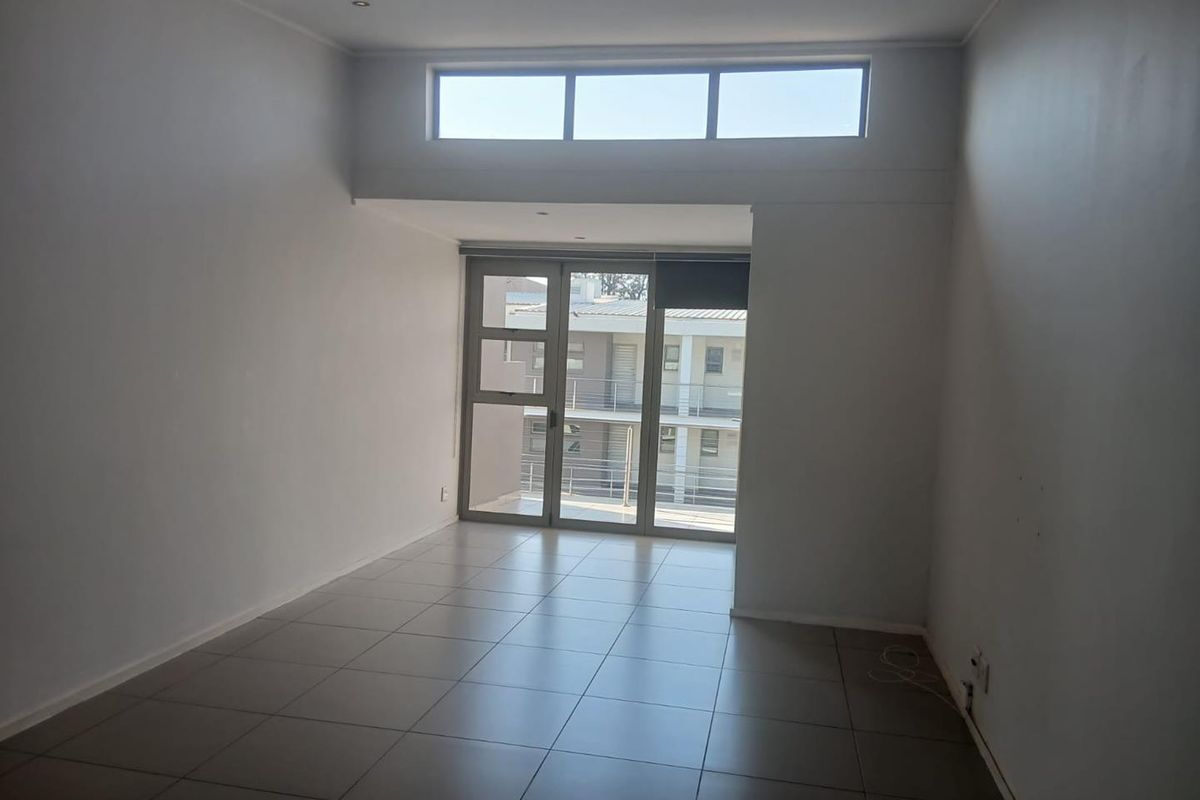 An empty, well-lit living area featuring neutral tiled flooring, recessed downlights, and large aluminium sliding doors leading to an outdoor space.