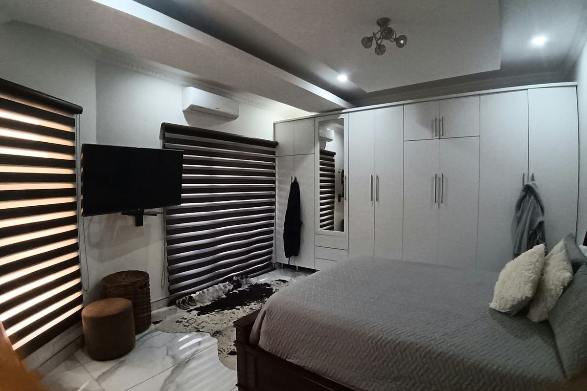 Spacious bedroom featuring built-in wardrobes, modern marble-look flooring, recessed ceiling lighting, and a wall-mounted air conditioning unit.