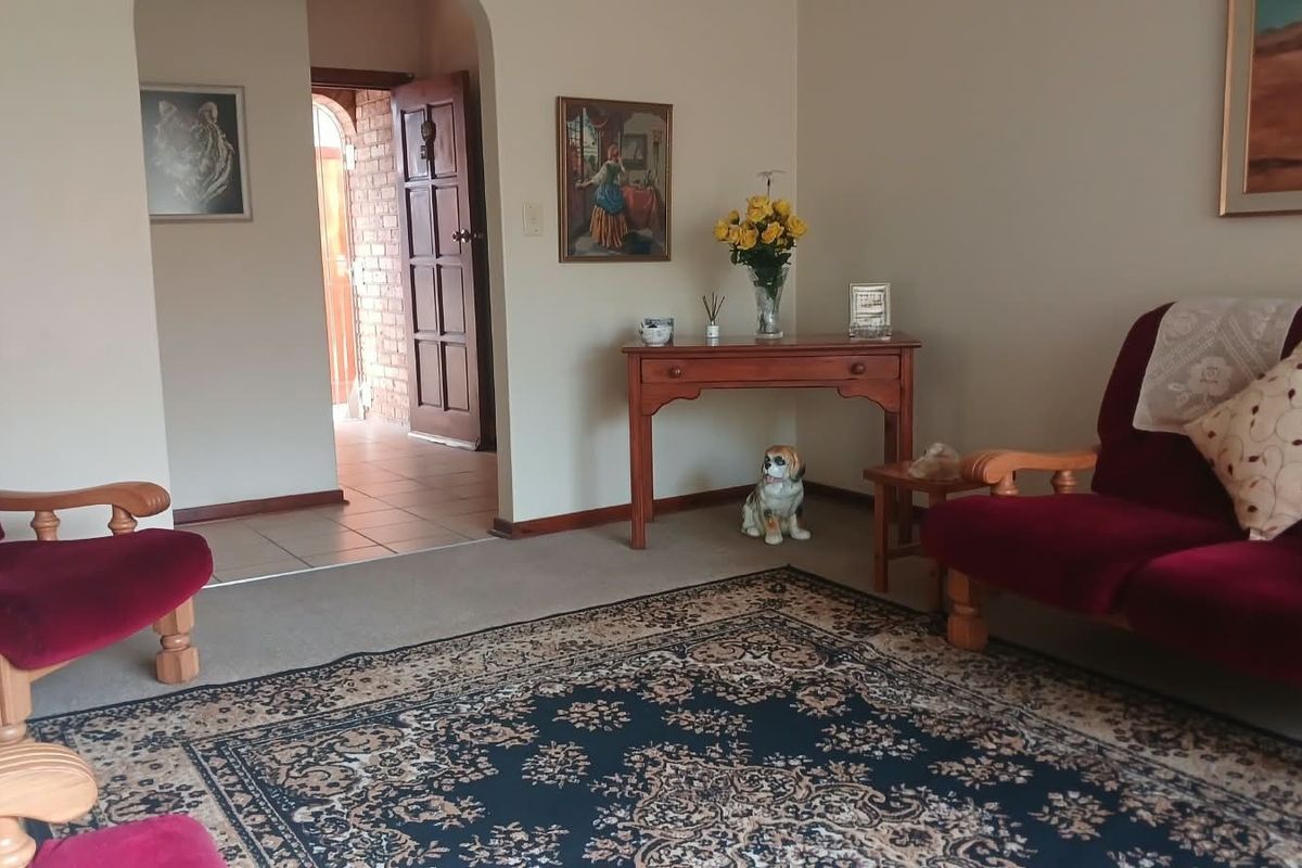 A living room area featuring carpeted flooring, an arched entryway, and a tiled transition area leading to a timber door.
