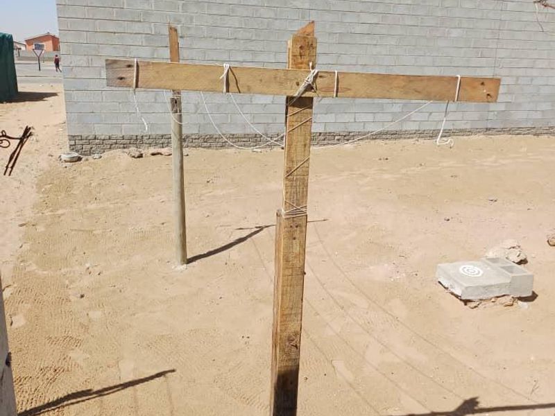 A rear yard area featuring a concrete block boundary wall and an unfinished sandy ground surface.