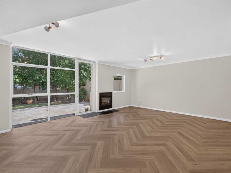 Spacious, light-filled living room featuring modern herringbone flooring, a built-in fireplace, and large glass doors providing seamless access to the outdoor area.