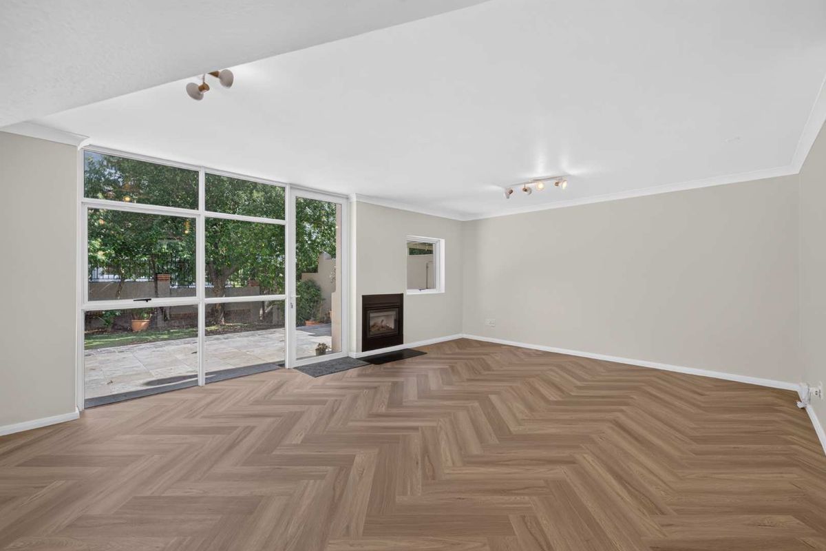 Spacious, light-filled living room featuring modern herringbone flooring, a built-in fireplace, and large glass doors providing seamless access to the outdoor area.