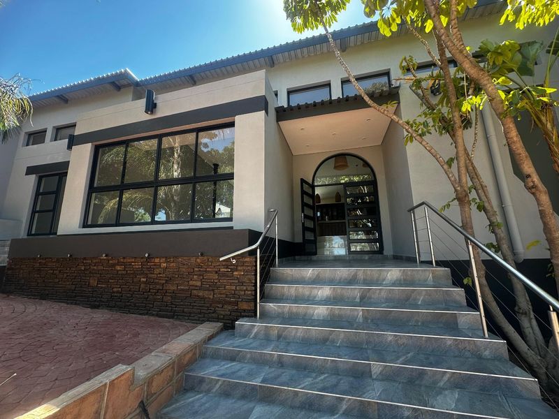 Modern front entrance featuring a tiled staircase with stainless steel railings, stone cladding accents, and a striking arched glass-paneled front door.