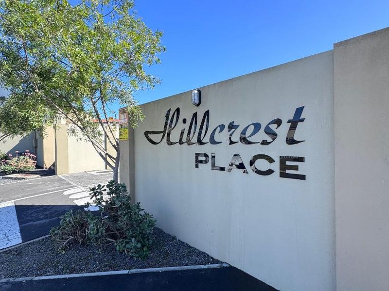 Entrance view of Hillcrest Place complex featuring a boundary wall with signage and exterior lighting.