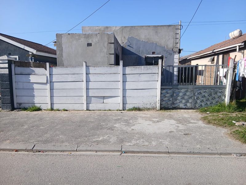 Front elevation of a residential property featuring a precast concrete boundary wall, metal gate, and an unfinished cement facade.