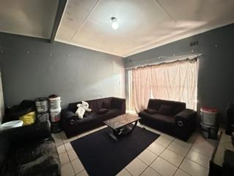 A living room featuring tiled flooring and a sliding glass door, currently showing signs of ceiling wear and paint deterioration.