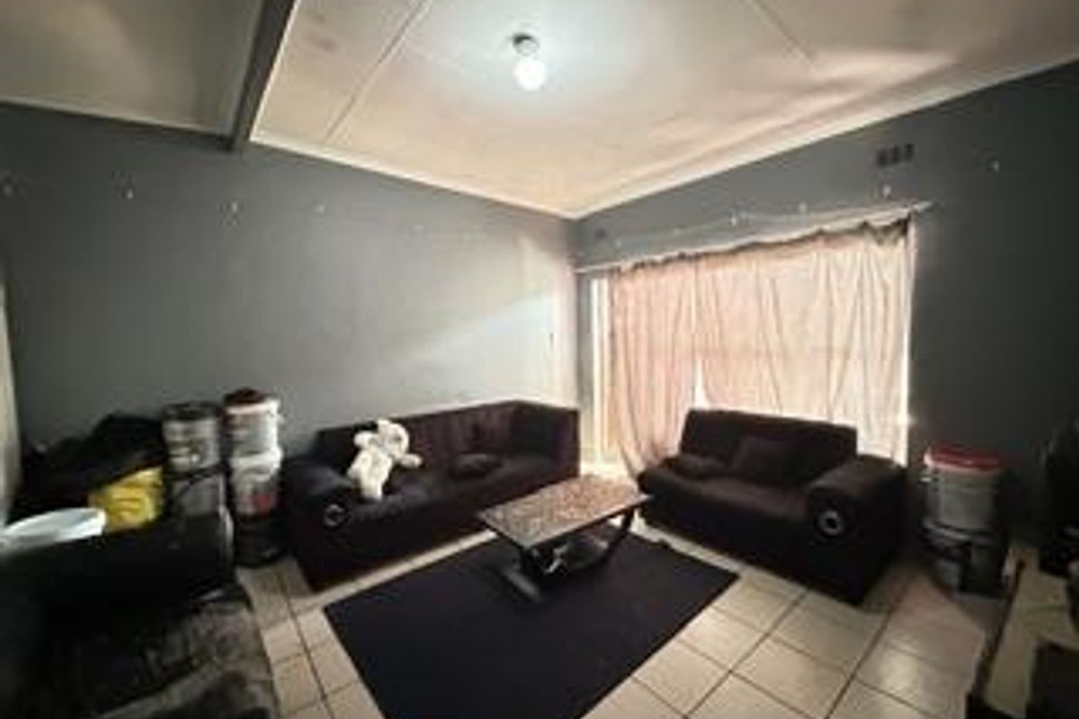 A living room featuring tiled flooring and a sliding glass door, currently showing signs of ceiling wear and paint deterioration.