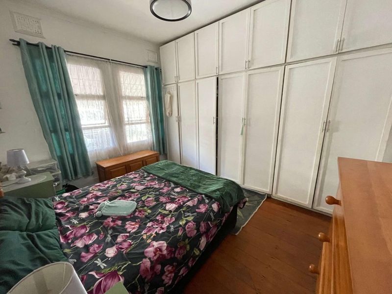 A bedroom featuring timber flooring and extensive built-in floor-to-ceiling white wardrobes providing ample storage space.