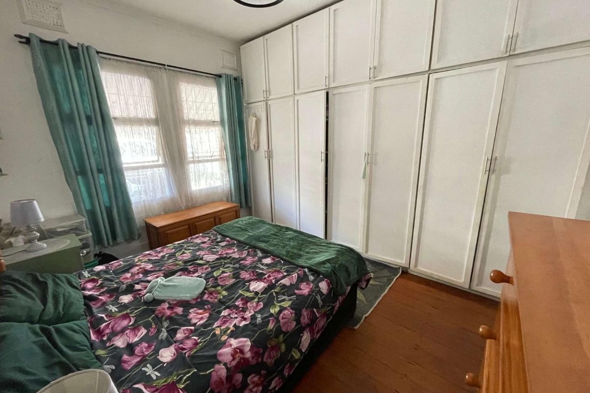 A bedroom featuring timber flooring and extensive built-in floor-to-ceiling white wardrobes providing ample storage space.