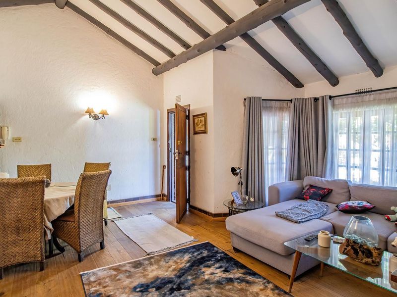 Open-plan living and dining area featuring vaulted ceilings with exposed timber beams, hardwood flooring, and direct access to the outdoors via sliding glass doors.