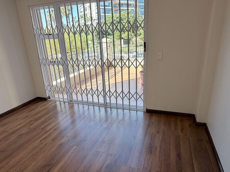 An empty living room featuring laminate flooring and a sliding glass door with a security gate leading to an outdoor patio area.