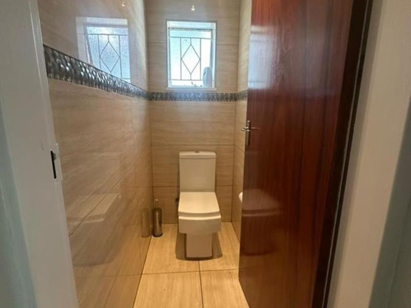 A compact, well-maintained guest bathroom featuring neutral ceramic wall and floor tiles, a modern toilet, and a timber door.