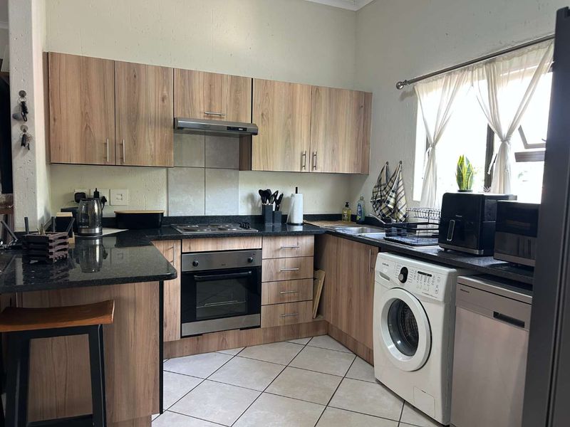 Functional kitchen featuring wood-look laminate cabinetry, granite countertops, built-in oven with extractor fan, and tiled flooring with space for under-counter appliances.
