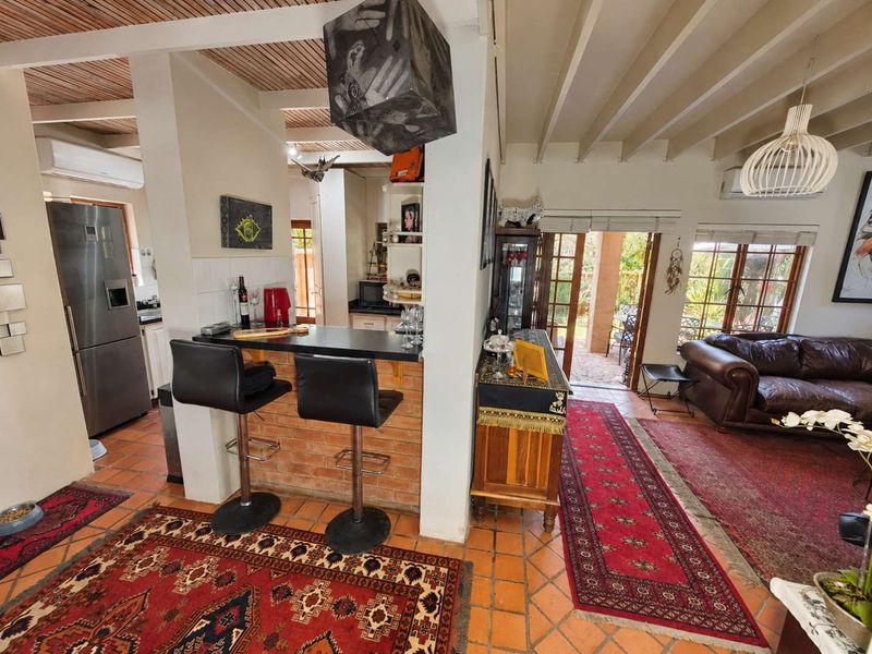 Open plan living and kitchen area featuring exposed timber beam ceilings, terracotta flooring, and a brick breakfast bar with direct access to the patio.