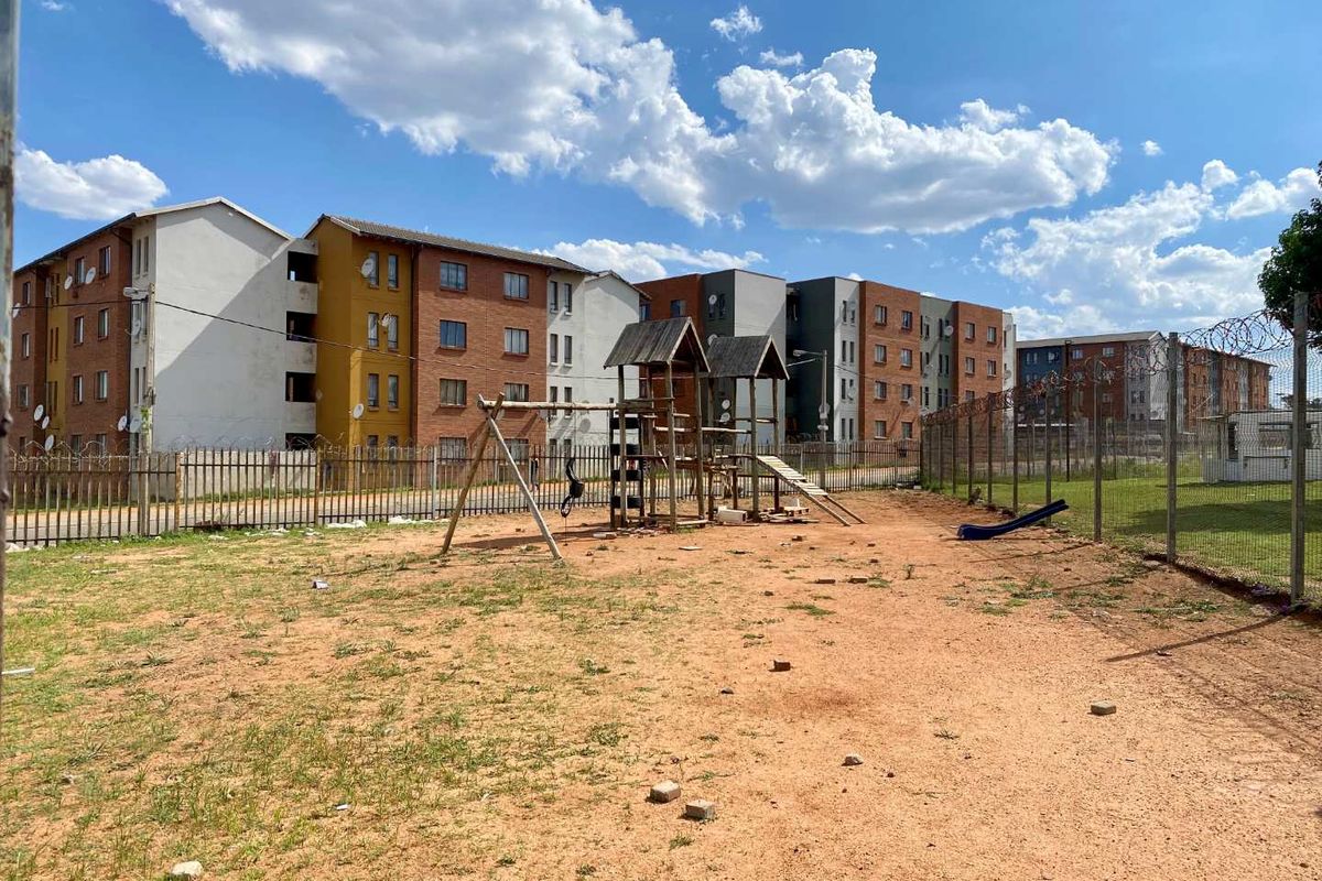 Outdoor communal area featuring a playground set within a fenced residential apartment complex.