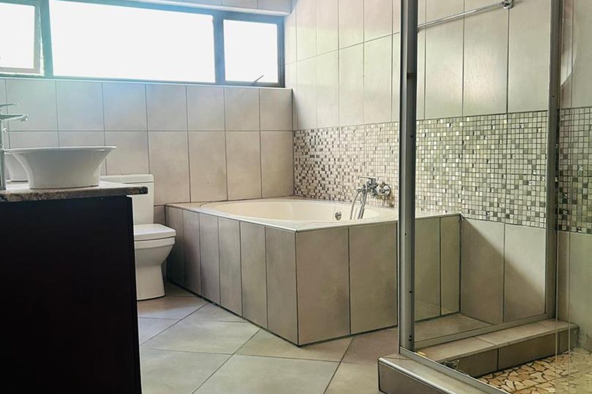 A functional bathroom featuring a built-in bathtub, a separate glass-enclosed shower, a vanity with a vessel sink, and neutral wall and floor tiling.