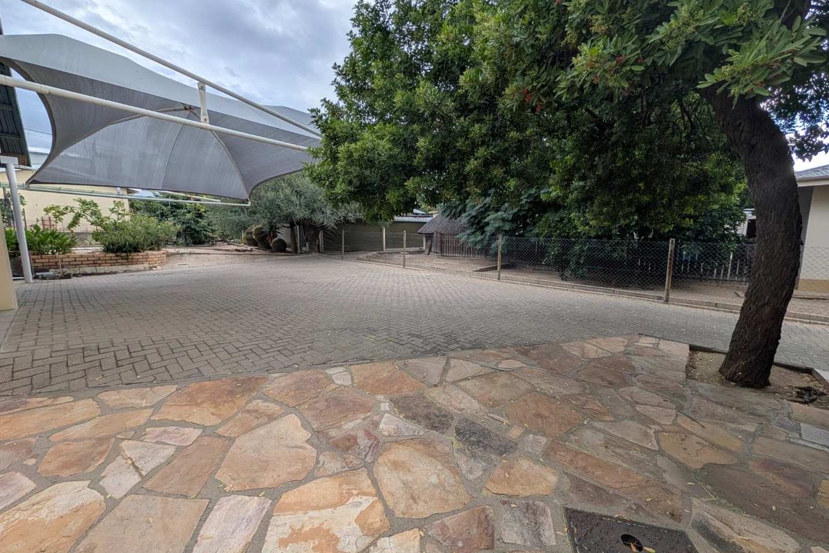 Spacious outdoor area featuring a combination of stone paving and interlocking brick driveway, shaded by a large tree and a structural shade sail.