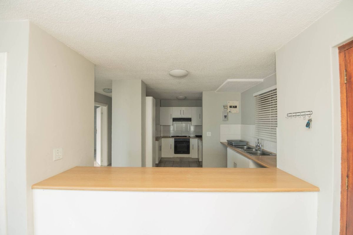 A functional kitchen featuring a breakfast bar, built-in oven, extractor fan, and stainless steel sink, with a neutral layout and direct access to adjacent rooms.