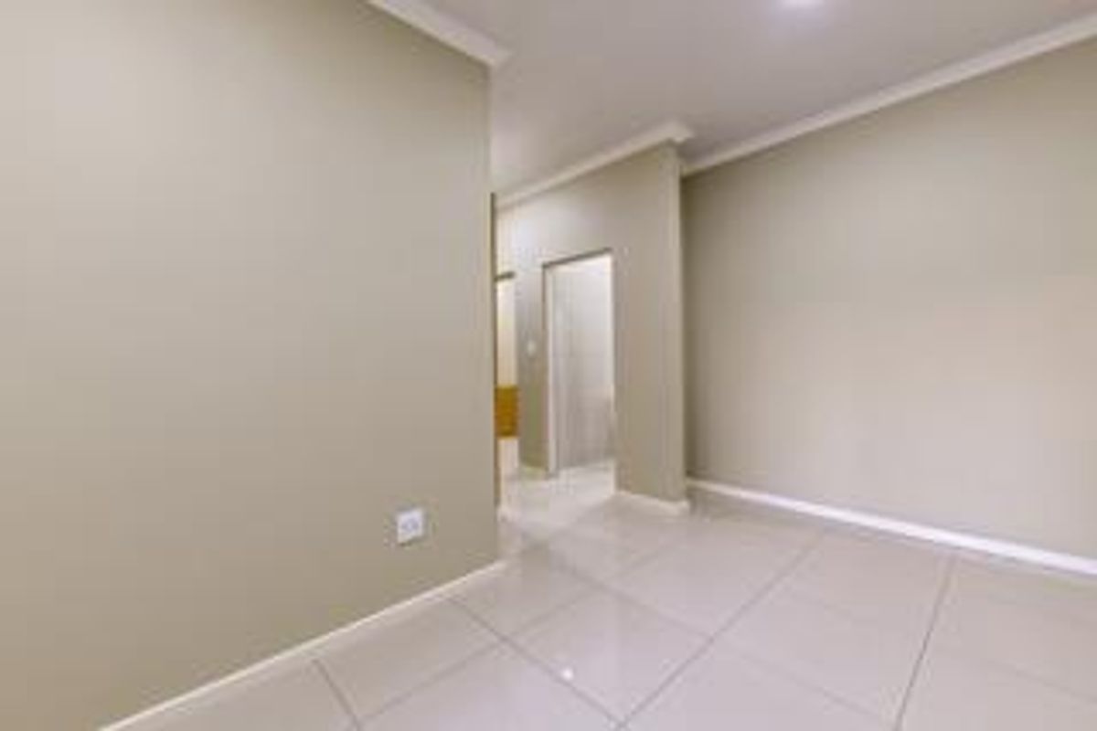 A bright, neutral-toned interior space featuring polished porcelain floor tiles, clean wall finishes, and a clear transition into an adjacent room.