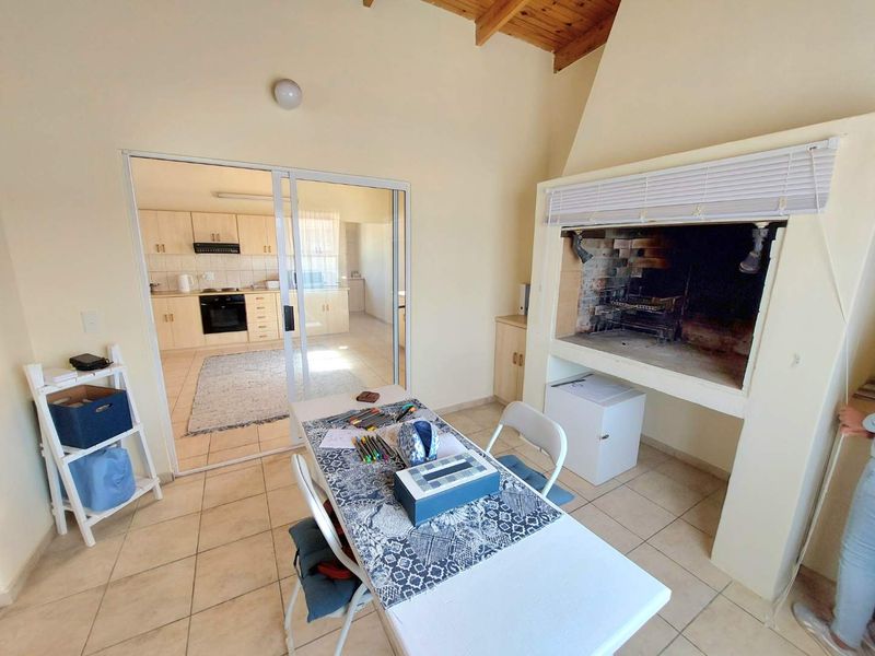 Open-plan living area featuring a built-in indoor braai, exposed timber ceiling beams, and direct access to a functional kitchen with built-in cabinetry.