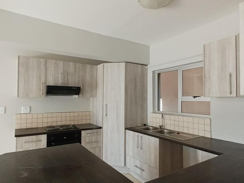A clean, modern kitchen featuring light wood-grain cabinetry, dark countertops, a built-in oven with hob, and a double basin sink.