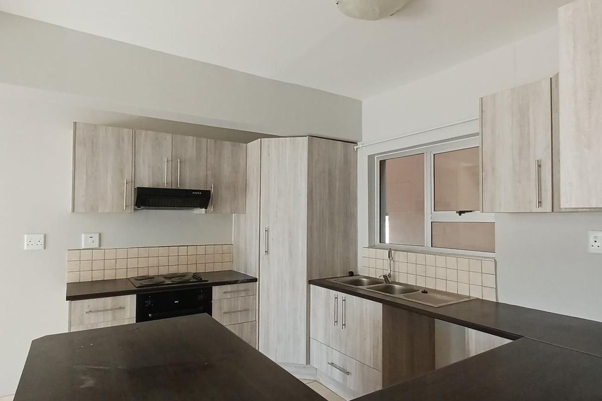 A clean, modern kitchen featuring light wood-grain cabinetry, dark countertops, a built-in oven with hob, and a double basin sink.