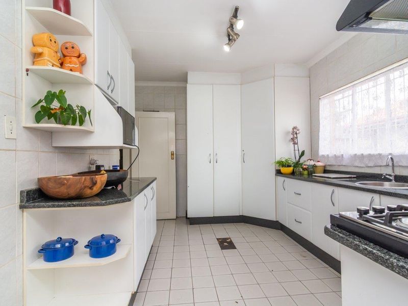 A functional kitchen featuring white cabinetry, granite countertops, a gas hob, and tiled finishes throughout.