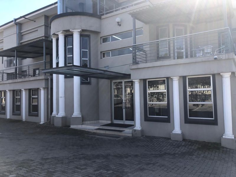 Front facade of a multi-story office building featuring decorative columns, glass entrance, and balcony areas with stainless steel railings.