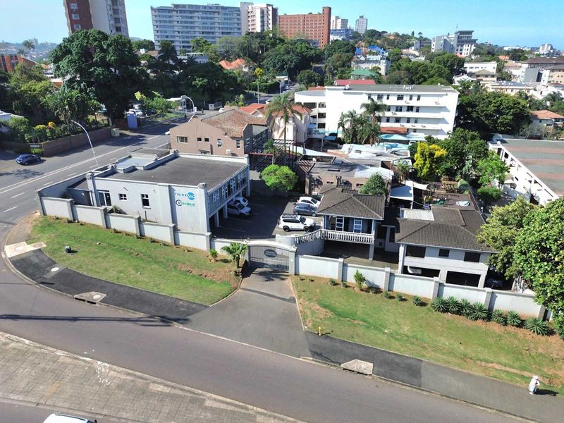 Aerial view of the property showing the building layout, perimeter wall, security gate, and paved driveway access from the street.