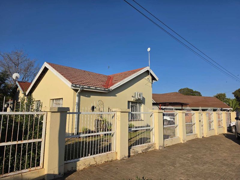 Front exterior view of a single-story house featuring a tiled roof, perimeter wall with metal fencing, and an installed air conditioning unit.